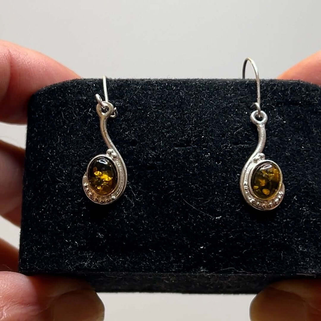 Green amber drop dangle earrings with sterling silver accents displayed on black holder.