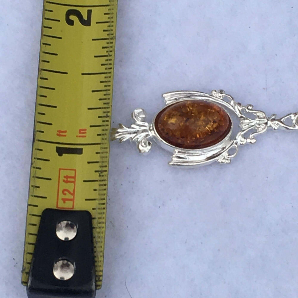 Sterling silver and cognac amber earring next to measuring tape indicating size of the drop dangle design.